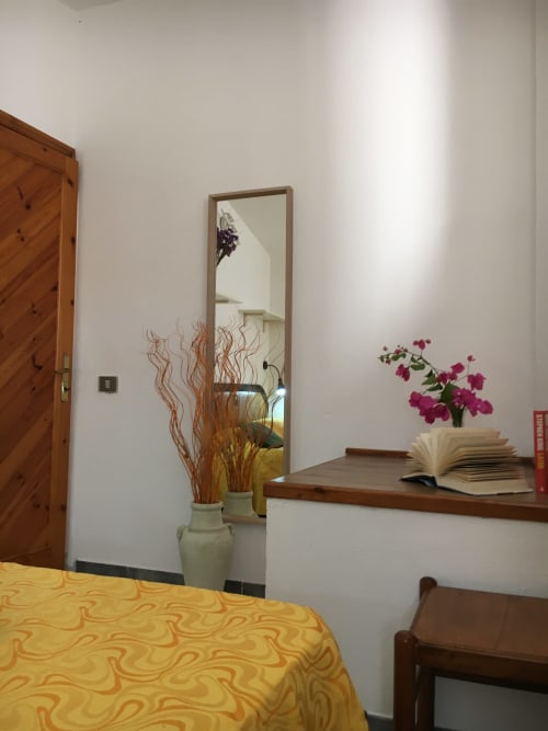 Camera da letto presso Loddo Paola a Orosei con mobili in legno, specchio, copriletto a motivi gialli e fiori freschi sulla scrivania