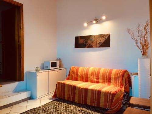 Luminoso soggiorno di Casa Arborea a Orosei con divano letto rigato, mobili bianchi e arredamento moderno