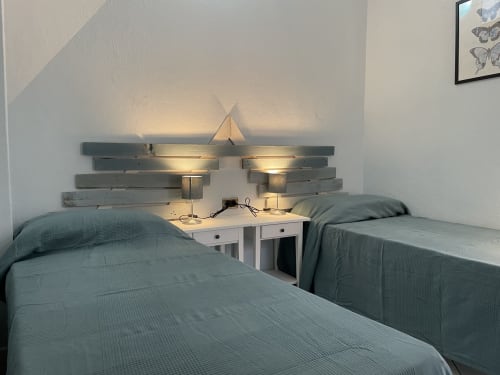 Twin bedroom with teal bedding, wooden headboard with sconces, and nightstand at Loddo Paola apartment in Orosei, Italy