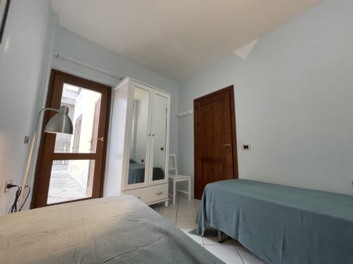 Bright bedroom in Orosei apartment with two beds, wardrobe, dark wood doors, and veranda access