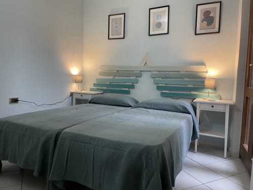 Modern bedroom in Orosei apartment with teal bedding, white nightstands, turquoise headboard wall art, and accent lighting