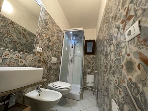 Modern bathroom in Orosei apartment with patterned tile walls, white fixtures, shower cabin, and vessel sink