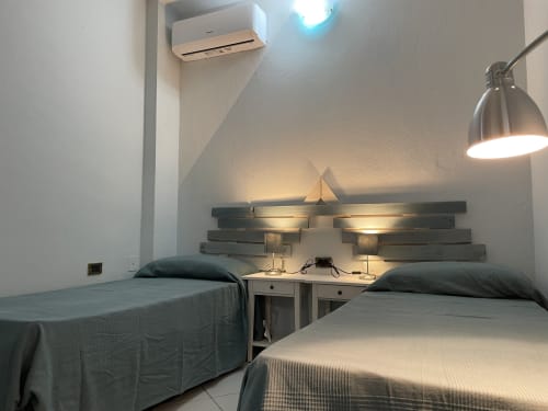 Two twin beds with dark pillows in modern Orosei apartment, featuring wooden headboard and wall-mounted lamps