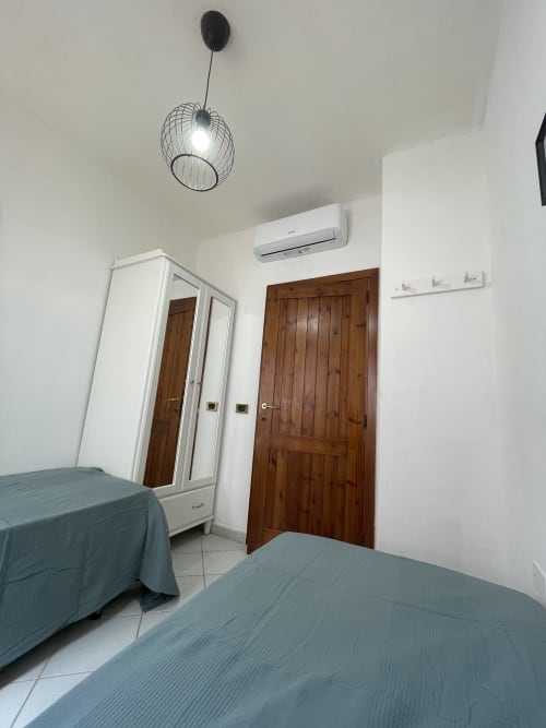 Modern bedroom in Orosei apartment with twin beds, wardrobe, AC unit, and contemporary pendant lighting