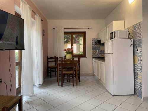 Open-plan kitchen and dining area in Orosei apartment with white appliances, wooden table, and patio doors with garden view