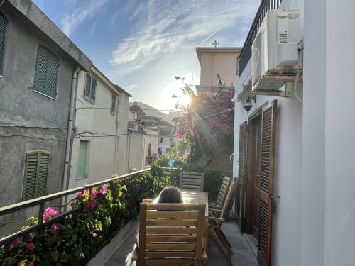 Sunny veranda with pink bougainvillea flowers, wooden furniture, and charming Orosei townhouses in background