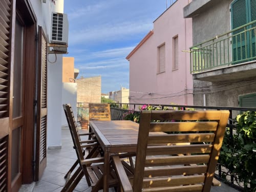 Sunny terrace with wooden furniture overlooking colorful buildings in Orosei, Italy apartment rental