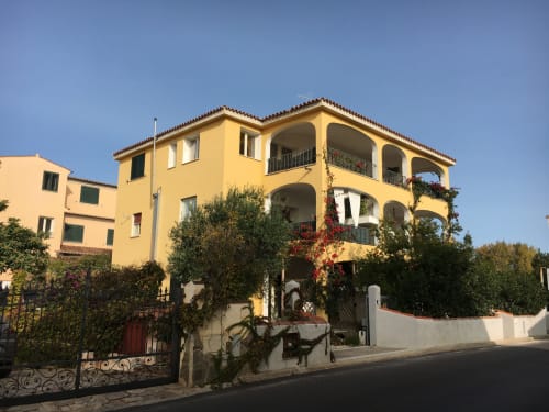 Yellow Mediterranean villa in Orosei with arched balconies, ivy-covered walls, and red flowers climbing the facade