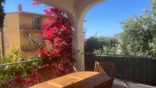 Sunny veranda with wooden table and chairs, vibrant pink bougainvillea, Orosei apartment balcony view
