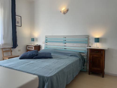 Modern bedroom in Orosei apartment with turquoise wood headboard, blue bedding, and dark wood nightstands