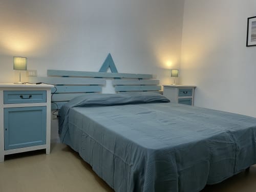 Modern bedroom with turquoise bed frame and nightstands, white walls, ambient lighting at Sa Domo De Mannoi apartment in
