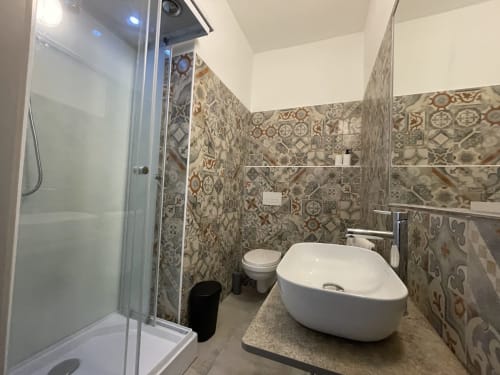 Modern bathroom with patterned tile walls, white vessel sink, toilet, and shower enclosure at Sa Domo De Mannoi apartment in