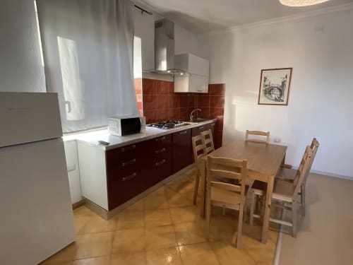 Modern kitchen-dining area with red tile backsplash, wooden table and chairs, stainless steel appliances, and terracotta