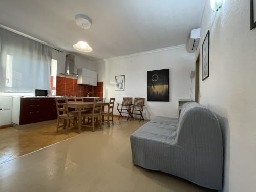 Modern apartment living area with red kitchen, wooden dining table, and gray sofa in Orosei, Italy