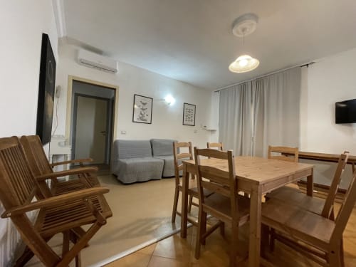 Modern apartment living room in Orosei with wooden dining table, chairs, gray sofa, TV, and air conditioning