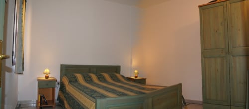 Camera da letto in Casa Arborea a Loddo Paola, Orosei con letto rigato, armadio in legno e lampade da comodino