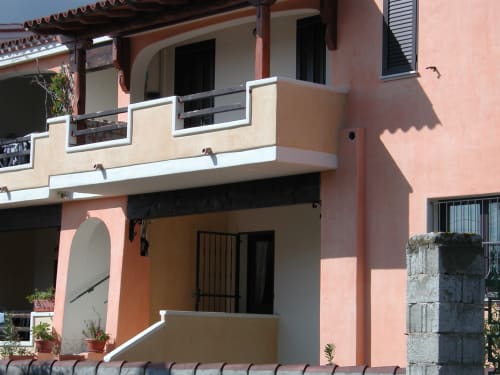 Villa sarda color corallo con tetto in laterizio, portico ad arco e balconata a Orosei