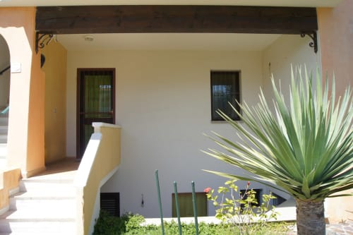 Ingresso di Casa Arborea G a Orosei con portico coperto, porte in legno, finestre e piante tropicali