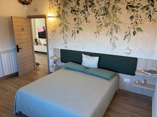 Camera moderna a La Dimora Di Ipno con letto matrimoniale, testata verde, murale botanico, pavimenti in legno e vista sul giardino