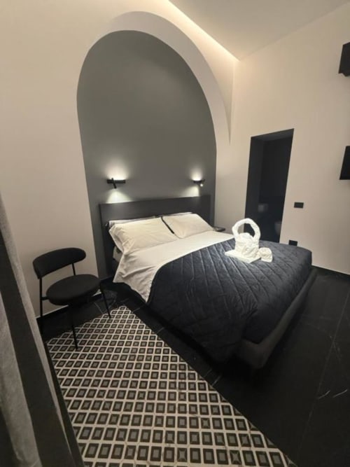 Camera da letto moderna a Volta 70 Napoli con nicchia ad arco, letto con struttura nera, biancheria bianca, pavimento decorato e illuminazione d'accento