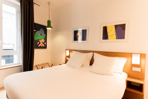Suite moderne à l'Hôtel Louvre Richelieu à Paris avec lit queen-size, tête de lit en bois, art abstrait, luminaire suspendu