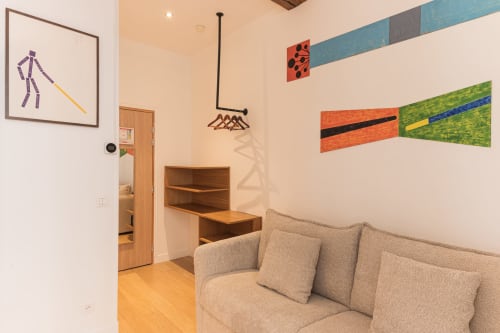 Suite moderne à l'Hôtel Louvre Richelieu Paris avec canapé beige, bureau en bois, art mural coloré et décoration contemporaine