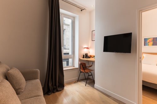 Suite moderne à l'Hôtel Louvre Richelieu à Paris avec coin salon, bureau, TV écran plat et vue sur fenêtre