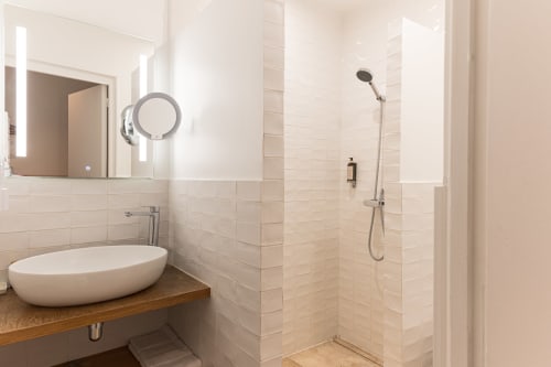 Salle de bains moderne à l'Hôtel Louvre Richelieu Paris avec lavabo rond, miroir lumineux et douche spacieuse
