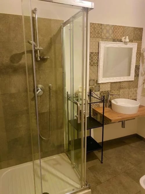 Bagno moderno al Corte Sicula B&B di Siracusa con doccia in vetro, mobile lavabo in legno e piastrelle decorative.