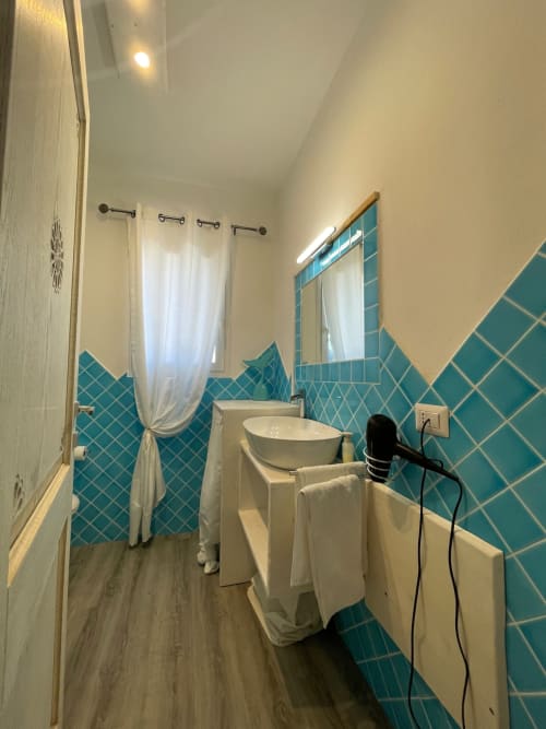 Bagno moderno con piastrelle turchesi, lavabo bianco, specchio e tenda doccia presso Villa Carrie Porto Pozzo