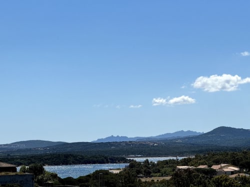 Vista panoramica di Porto Pozzo con acque cristalline, colline boscose e montagne sotto cieli sereni