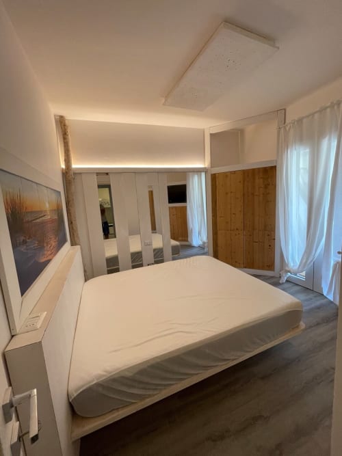 Camera da letto moderna a Villa Carrie Porto Pozzo con letto bianco, armadio specchiato, mobili in legno e illuminazione ambientale al soffitto