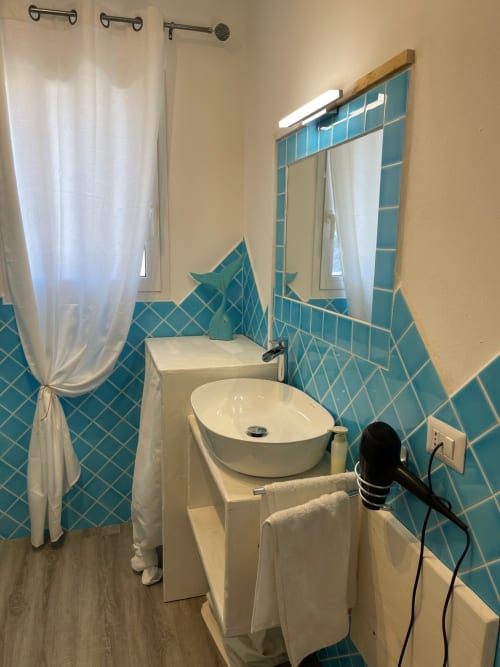 Bagno moderno di Villa Carrie Porto Pozzo con piastrelle turchesi, lavabo rotondo bianco e tenda doccia