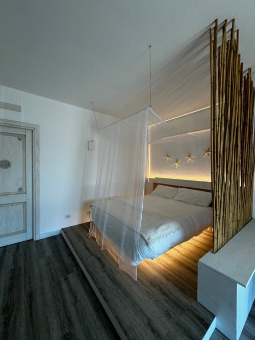 Camera da letto moderna di Villa Carrie Porto Pozzo con letto a baldacchino, tende trasparenti, divisorio in legno e illuminazione ambientale
