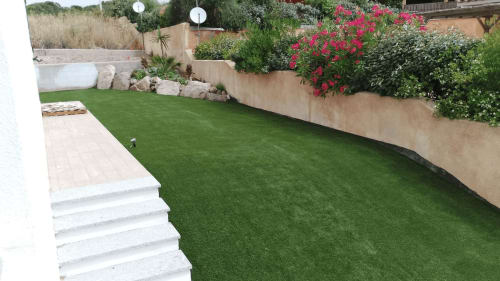 Giardino curato con erba sintetica, scalinata bianca, arbusti fioriti e muri di sostegno in pietra a Villa Carrie Porto Pozzo