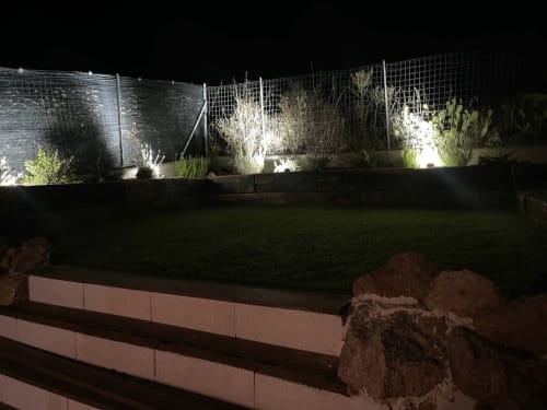 Giardino di Villa Carrie Porto Pozzo di notte con piante illuminate, prato verde e recinzione moderna
