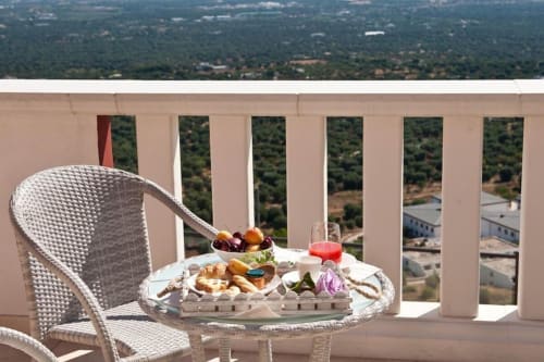 Breakfast spread on terrace table at Al Mirador Resort, Fasano, overlooking countryside landscape with wicker chair and sea