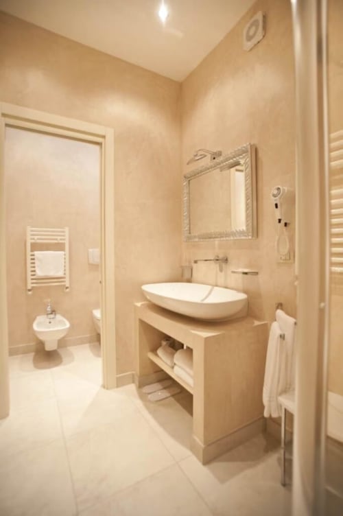 Modern bathroom at Al Mirador Resort with white vessel sink, decorative mirror, and beige marble walls
