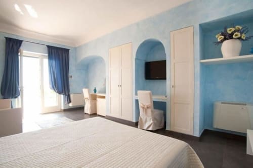 Geräumige Junior Suite im Al Mirador Resort in Fasano mit hellblauen Wänden, Queensize-Bett, weißen Kleiderschrankttüren und modernem Design