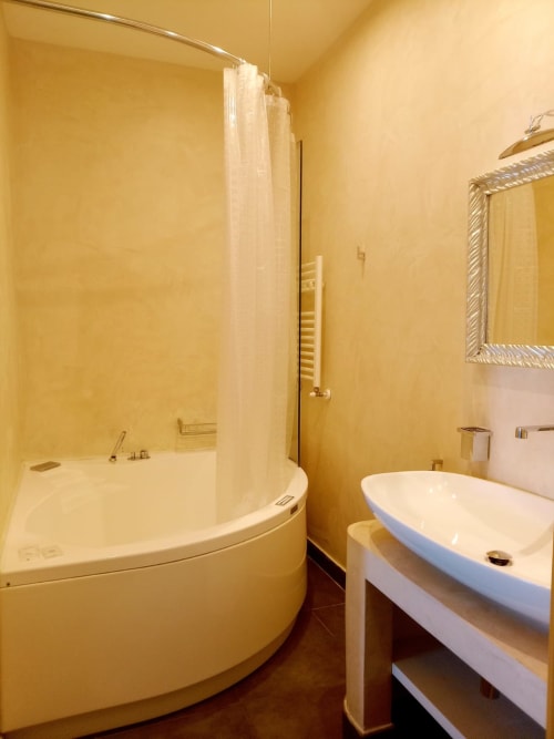 Modern bathroom with curved corner bathtub, shower enclosure, vessel sink, and warm yellow walls at Al Mirador Resort Fasano