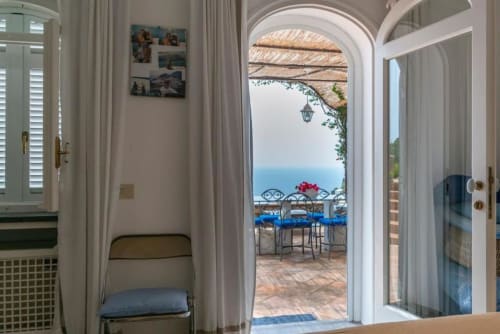Elegante camera d'hotel a Capri che si affaccia su terrazza con vista mare, portale ad arco e paesaggio costiero mediterraneo
