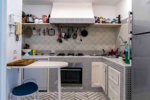 Cucina moderna compatta a La Conciergerie Capri con mobili bianchi, piastrelle decorative e ripiani aperti.
