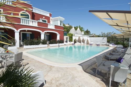 Poolbereich des Al Mirador Resort in Fasano mit rotem Gebäude, Liegestühlen und mediterraner Architektur