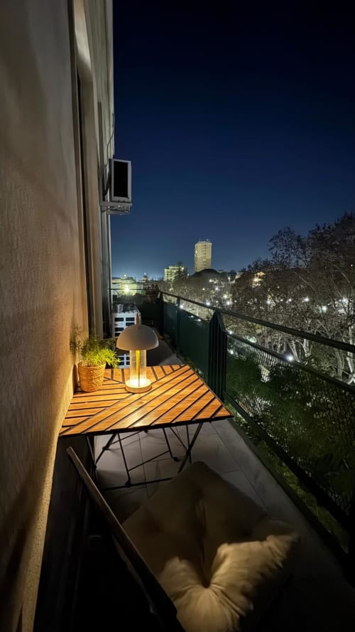 Balcone illuminato di notte con terrazza in legno, lampada a fungo e luci della città a Catania, Sicilia