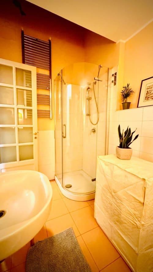 Bagno moderno con doccia, lavabo e bidet nell'appartamento Todo Sicily, Catania. Illuminazione calda, pavimenti in piastrelle, pianta in vaso.
