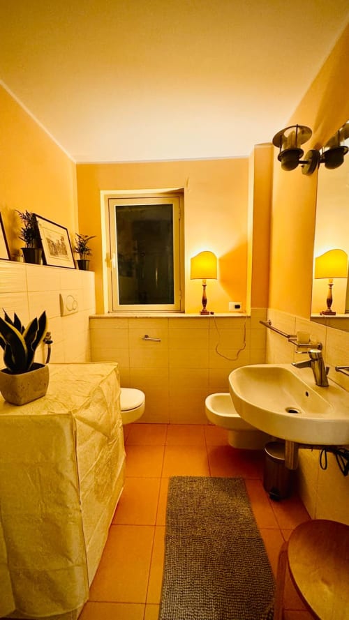 Bagno giallo luminoso nell'Appartamento Todo di Sicilia con doppio lavabo, WC, specchio, illuminazione calda e piastrelle in cotto