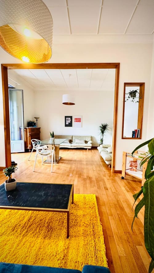 Soggiorno moderno a Catania con lampada a sospensione gialla, pavimenti in legno, tavolo da pranzo in vetro, layout aperto e piante decorative