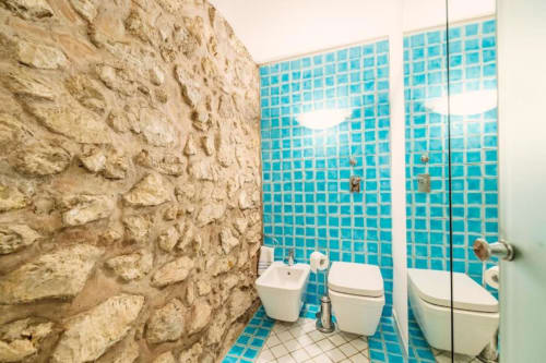 Bagno moderno di La Conciergerie Capri con piastrelle a mosaico turchese, muri in pietra e sanitari bianchi contemporanei
