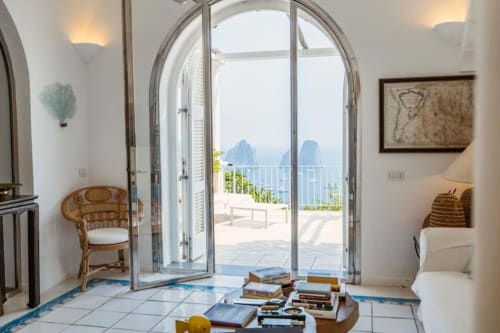 Elegante interno di villa a La Conciergerie Capri con porte ad arco che si aprono sulla terrazza con vista mare e lo scoglio iconico di Capri