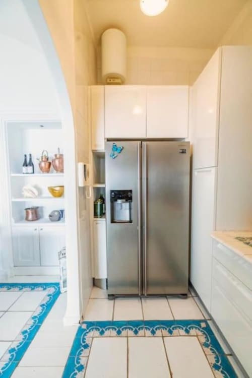 Cucina moderna con frigorifero in acciaio inox, mobili bianchi e piastrelle blu decorative della villa La Conciergerie Capri